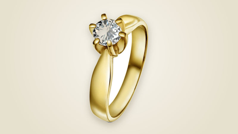Forlovelsesring i gult gull med en innfattet diamant, mot en varm, sandfarget bakgrunn